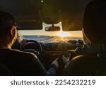 Small photo of A middle-aged couple driving a 4x4 from inside the car at dawn on a totally snowy road with the sun rising on the horizon and the driver's gaze reflected in the rearview mirror