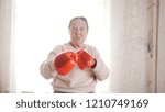 Small photo of An old senior women boxing in red gloves, looking aggressively funny