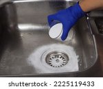 Gloved hand putting baking soda on drain in kitchen sink from glass jar. Close up. Eco friendly house cleaning concept.