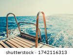 
Ladder on deck of sailing yacht above rippled blue water in bright sunlight.
Boat dock with ladder and lake background. River background with dock ladder