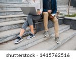 legs in footwear of man and woman sitting on stairs in urban city center in smart casual business style working together on laptop wearing sneakers, stylish freelance people using technology outside