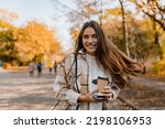 candid attractive young smiling woman walking in autumn park with coffee wearing checkered coat, happy mood, fashion style trend, long brown hair