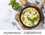 Spinach and cheese omelette. Frittata made of eggs, paprika and spinach in a frying pan on a marble countertop. View from above. Copy space.