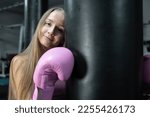 Small photo of Long-haired boxer girl in pink boxing gloves hugs a black projectile - a concept of sports activity