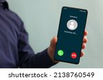Small photo of Male hand holding a smartphone with unknown caller displayed on screen. Unknown caller telephony concept. Incoming call at mobile phone. Prank caller, scammer or stranger, privacy, fraud, cybercrime.