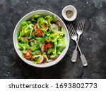 Easy vegetarian vegetable salad with fresh vegetables. Cherry tomatoes , romano lettuce, cucumbers, radishes and french mustard, olive oil, lemon salad dressing on a dark background, top view         