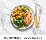 Small photo of Delicious food - roasted potatoes, chicken breast, grilled zucchini and arugula spinach salad on a dark background, top view
