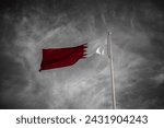 Small photo of Doha, Qatar-‎February 24,2024 : The Qatari flag flies above the flag bearer in colors, with the black and white sky in the background