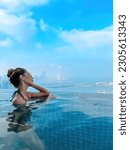 Small photo of Beautiful brunette girl in a swimsuit with a slender figure, plump lips, in sunglasses. A girl in an infinite pool against the backdrop of a beautiful city. Sky clouds sea, vacation beach summer Dubai