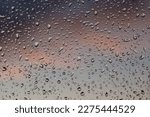 Window glass after rain. Drops of water cover it from the outside. Blurred, indistinct, evening clouds can be seen in the background. They have red and navy blue color.