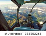 Helicopter cockpit flying on mountain landscape and cloudy sky, with pilot arm driving in cabin. Spectacular aerial view of Alps.