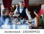 Smiling waiter serving fancy dishes to mature couple sitting at table in restaurant