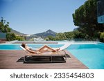 Small photo of Woman sunbathing on lounge chair next to luxury swimming pool mountain view