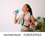 A young attractive woman stays hydrated after yoga session - glass water bottle