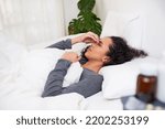 A young multi-ethnic woman holds her nose in pain lying in bed with migraine