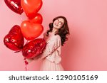 Laughing girl holding bunch of heart shaped party balloons. Studio portrait of wonderful ginger lady isolated on pink.
