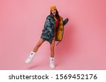 Full length view of girl in down jacket and winter boots. Studio shot of blissful brunette woman dancing on pink background.
