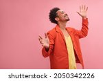 Small photo of Medium shot of happy African young and smiling man with closed eyes with copy space. Well dressed in fall colors with arms raised at his sides against solid pink background.