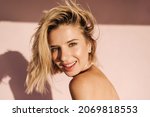 Close up portrait of fair skinned young woman looking at camera with mouth open. Blonde with short hair on one side on pink background with bare shoulders. People sincere emotions lifestyle concept.