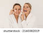 Two funny caucasian women in bathrobes and blindfolds spend weekend at spa. Blonde girls take care of their skin face. Beauty concept
