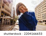 Small photo of Pretty young caucasian woman closing her eyes smiles teeth walking around city. Brown-haired with bob haircut wears blue sweatshirt. Positive emotions concept
