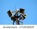 Closeup of top of tall strong metal structure holding four large public civil defence warning air sirens on clear blue sky background