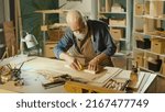 Small photo of Professional Elderly Man Carpenter Working on Wood Using Carpentry Tools in the Garage. Craft Authentic Workshop. Handicraft, Creative Small Business. Profession, Art and Hobby Concept.