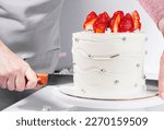 woman cuts pastry knife wedding cake with white chocolate ganache and silver decorations with fresh strawberry on top. Celebrates March 8. Homemade baking, hobby and delicious dessert, selective focus