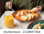 Macro closeup of woman sitting at breakfast table holding eating potato fried hash browns with hand on plate by glass of chocolate milk and background of phone