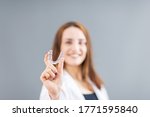 Small photo of Beautiful smiling Turkish woman is holding an invisalign bracer in a studio with grey background