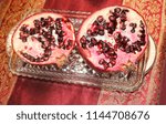Small photo of A pomegranate cut in two on a cut glass dish and a maroon and gold cloth