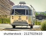 Small photo of 2021_06_04 Grand Junction Colorado USA - Airstream camper trailer parked on concrete with grape vineyards and mesa and barn behind it.
