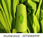 Small photo of GreenSustainable Fashion: Leaf on a green yarn cone with a backdrop of a green fabric, symbolising sustainability