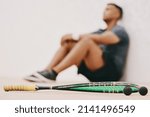 Small photo of Just because youre beat doesnt mean youre beaten. Shot of a young man taking a break after playing a game of squash.