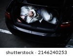 Small photo of Hoping for a miracle. A bound and blindfolded businessman lying in the trunk of a car.
