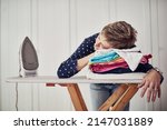 Housework is hectic. Shot of a woman with her head down on a pile of clothes on an ironing board.