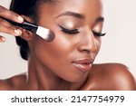 Small photo of Brush on more of your beauty. Studio shot of a beautiful young woman applying blush with a makeup brush.