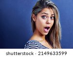 Small photo of What a shocker. Portrait of a shocked young woman isolated on blue.