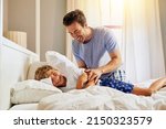 Small photo of Wake up sleepy head. Shot of a cheerful young man trying to wake up his son from sleeping on a bed at home in the morning.