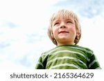 Cute young boy smiling. Low angle view of cute young boy standing against sky and smiling.