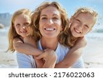 Small photo of Portrait of a cheerful mature woman and little girls enjoying family time at the beach on vacation. Happy sisters smiling with adopted mother, grandma or foster parent, enjoying fresh summer air