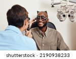 Optical exam, optician or eye doctor at work testing vision or sight of patient at optometrist. Happy, smiling young man checking his eyes for glasses or treatment at an ophthalmologist in a clinic.