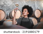 Small photo of Black woman tasting wine at a winery, looking and checking the color and quality of the years produce. Young African American sommelier proud of the new addition, analyzing white wine in a cellar