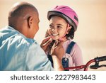 Small photo of Bike safety, kid and helmet of a girl with father ready for cycling learning outdoor with a smile. Dad with happy kid putting on safe gear for a bicycle teaching lesson with happiness and care