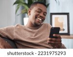 Small photo of Happy, phone and man in a living room texting, laughing and reading social media post in his home. Day off, black man and online chat on smartphone, text and funny message on dating website or app