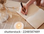 Hand, candle and woman writing in journal with top view for calm, peace mindset and relax morning routine in home. Hands, notebook and diary planning goals, idea vision or creative writer lifestyle