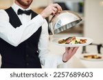 Small photo of Waiter, hands and opening plate of food for serving, meal or customer service at indoor restaurant. Man employee caterer or server catering or bringing open dish for fine dining, hospitality or order