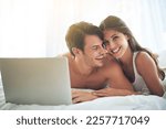 Laptop, happy and couple lying in bed together while watching a online movie or video at their home. Happiness, smile and portrait of a woman browsing the internet on computer with husband in bedroom