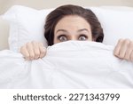 Small photo of Something went bump in the night...A young woman peeking out from under her ned sheet with a frightened expression.