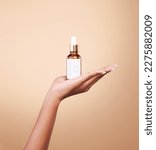 Small photo of Hand, product and antiaging serum with a woman in studio on a beige background to promote skincare. Marketing, advertising and luxury with a female holding a bottle for the promotion of beauty